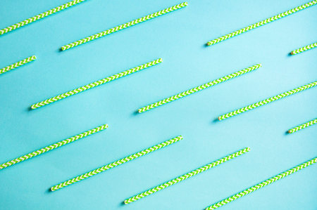 disposable green and white straws are laid out on a background of blue paperの写真素材