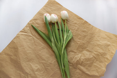 gift bouquet of white tulips lies on kraft paper on white paper background