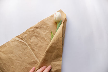 bouquet of white tulip flowers is wrapped by the girl's hand in craft paper on a white paper backgroundの写真素材