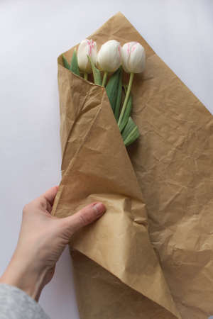 bouquet of white tulip flowers is wrapped by the girl's hand in craft paper on a white paper backgroundの写真素材