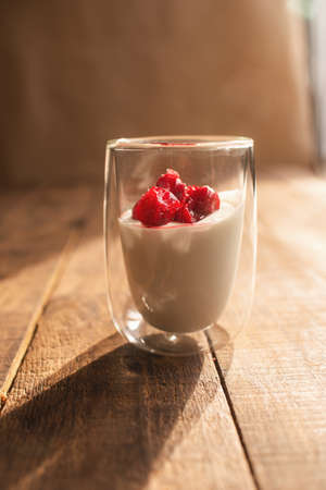 double glass with yogurt and berries on a wooden table where the bright sun is shiningの写真素材
