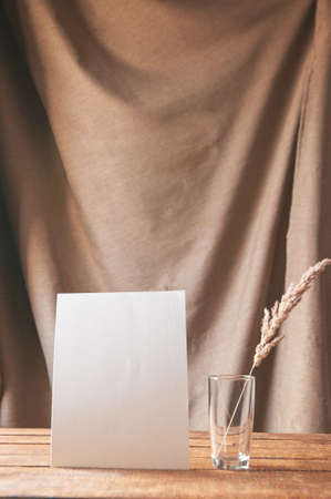 On the table is a white sheet of paper with dried flowers in a glass. For a design presentation or portfolio.の写真素材