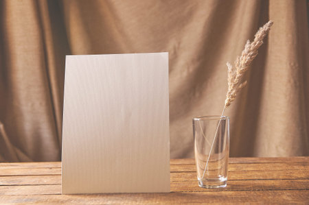 On the table is a white sheet of paper with dried flowers in a glass. For a design presentation or portfolio.の写真素材