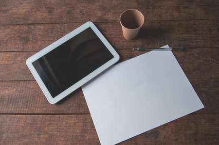 Office workplace with tablet pc on the table. On the table there is a tablet and a white sheet of paper with a pen. For a design presentation or portfolio.の写真素材