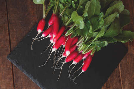 fresh radish with stems and leaves lies on a black granite pedestal boardの写真素材