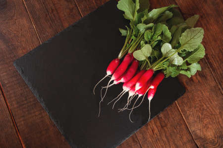 fresh radish with stems and leaves lies on a black granite pedestal boardの写真素材