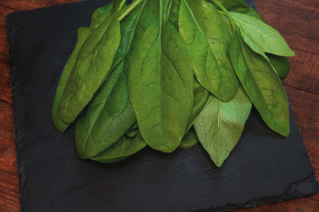 fresh spinach lies on a black presentation board located on a brown wooden table