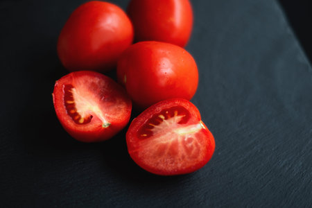 group of tomatoes, one cut in half, rests on a black board for servingの写真素材
