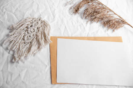 Envelope, macrame, pampas grass. Simple minimal flat lay on white textile with dry earth color neutral beige with macrame and dry reeds, pampas grass.の写真素材