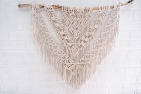 Handmade macrame 100 cotton wall decoration with wooden stick hanging on a white wall. DIY boho home...