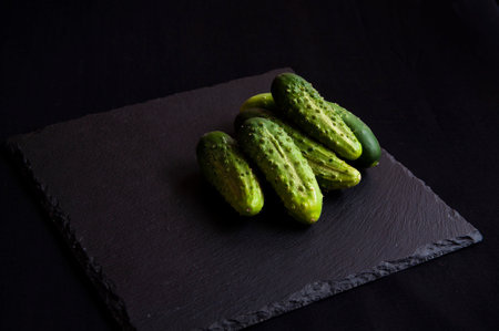 Natural fresh green cucumbers from a home garden on a black background, a dummy board made of stone. View from above.の写真素材