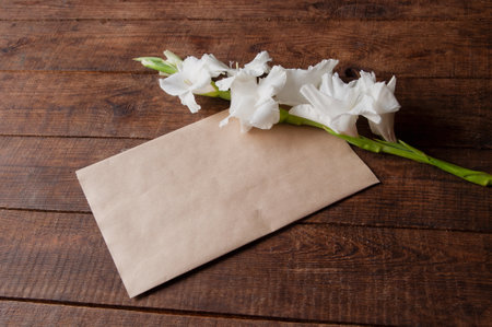 bouquet of white gladioli on a wooden table with an envelope in vintage styleの写真素材