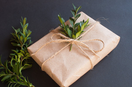 Craft gift box with knot natural with green leaves on black background. Sale concept on dark backgroundの写真素材