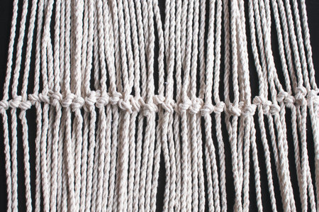 Macrame ornament from white natural cotton threads on a black background. Hand weaving from yarn on...