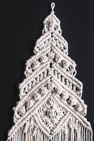 Christmas tree ornament macrame from white natural cotton threads on a black background. Festive...