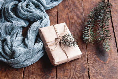 Gift box next to vintage tablecloth gray and christmas tree leaves on wooden brown table, festive composition on natural backgroundの写真素材