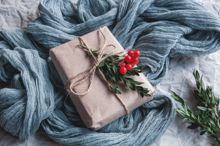 Gift box next to vintage tablecloth gray and spruce leaves with red berries on a white background,...