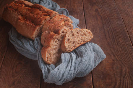 Sliced bread on a wooden table with a gray gauze tablecloth, fresh baguette on a wooden backgroundの写真素材