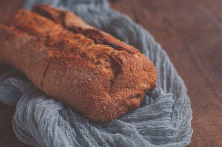 Bread on a wooden table with a gray gauze tablecloth, fresh baguette on wooden backgroundの写真素材