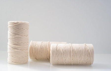 macrame threads wound bobbins of natural beige color are located on a light background