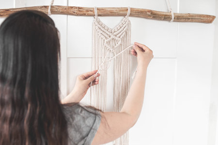 girl weaves a macrame pattern from natural white cotton threads for a large wall panel