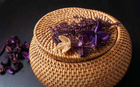 wicker straw box craft round top with dried flowers and lavender on a black backgroundの写真素材