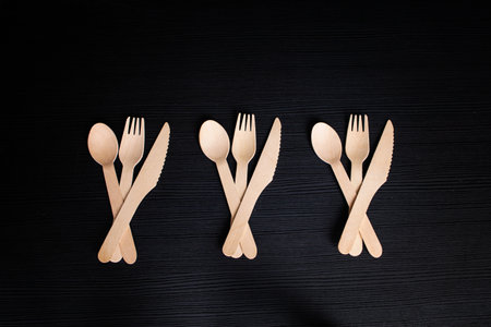 disposable eco-friendly wooden spoons, forks and knives on a dark backgroundの写真素材