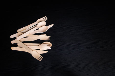 disposable eco-friendly wooden spoons, forks and knives on a dark backgroundの写真素材