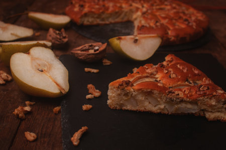 pear pie on a black serving board on a wooden table, cut pears and walnuts lie chaoticallyの写真素材