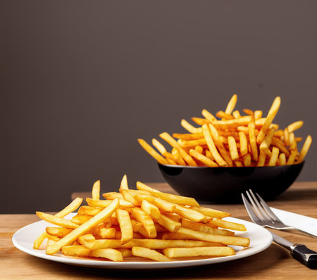Golden French fries potatoes on a white plate with fork and knife on wooden table