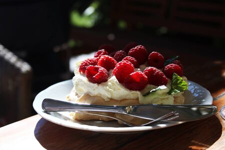 Piece of meringue cake with raspberries. On a white plate with knife and forkの写真素材