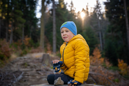 Little kid is sitting on a big stump on the mountain trail, eating. fall seasonの写真素材