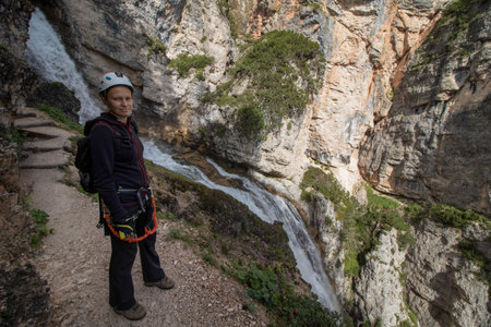 A woman standing on a trail in the Dolomites with a waterfall in the background. Dolomites, Italyの写真素材