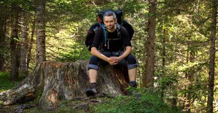 A man sitting with a backpack on a tree trunk by the trail. Dolomites, Italyの写真素材