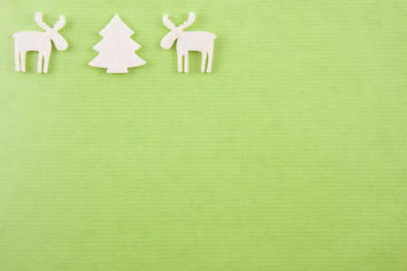 two white felt reindeers next to a white felt christmas in the left upper corner on a bright green paper backgroundの写真素材