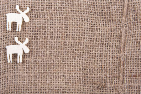 two white felt reindeer in the left upper corner on juteの写真素材
