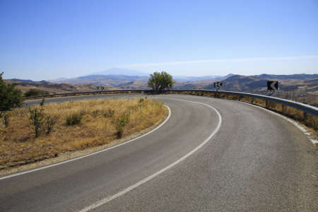 a bending asphalt road to new places with a nice view over the hilles and mountainsの写真素材