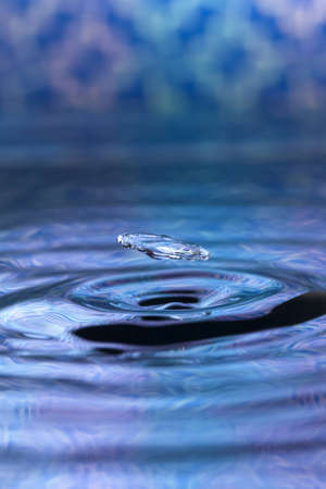 A blue abstract background of a close up of transparent water drops falling in water, making beautifull ripples and flowing waves in the surface and showing the pure energy it creates. Small depth of field.の写真素材