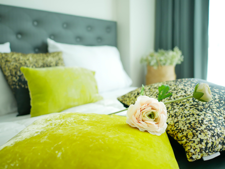 Romantic bedroom in blurred background, Closeup pink rose and colorful pillows on white bed with highlight from windowの写真素材