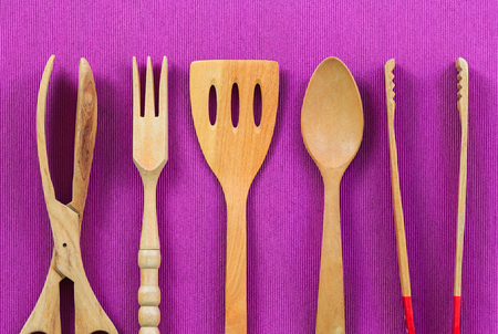 Isolated wooden kitchen utensils, Spoon, fork, clamp and flipper on purple tablecloth background
