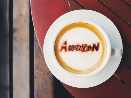 BANGKOK THAILAND-July 7 2019 : Top view cappuccino coffee with text amazon brand name topping by coffee powder in white ceramic cup on wooden table backgroundのeditorial素材