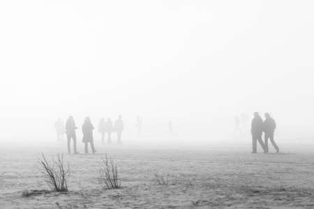 People in coats walking along the foggy beach, soft focusの写真素材