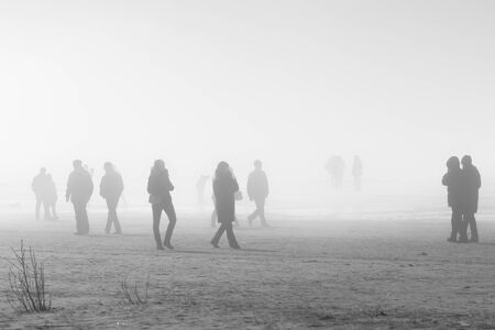 People in coats walking along foggy beach, soft focusの写真素材
