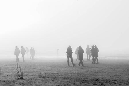 People in coats walking along the foggy beach, soft focus