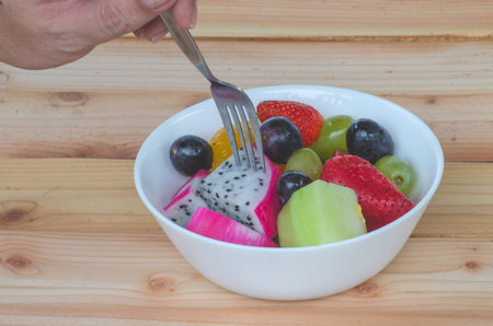 mixed fruit in white bowl on wood table, healthy foodの写真素材