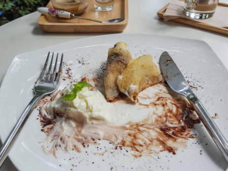 Remains of banana crape with chocolate syrup in white plate on white tableの写真素材