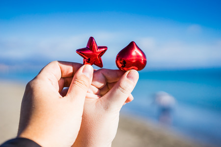 Two hands holding Christmas red and star against of blue sky and seaの写真素材