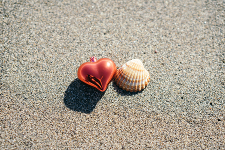 Close-up of red Christmas heart and seashell on sandの写真素材