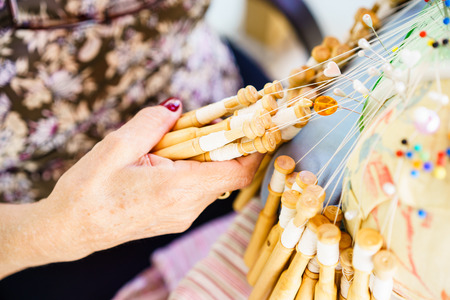 Unrecognizable senior woman with red nails weaving with bobbins and threads in close-upの写真素材