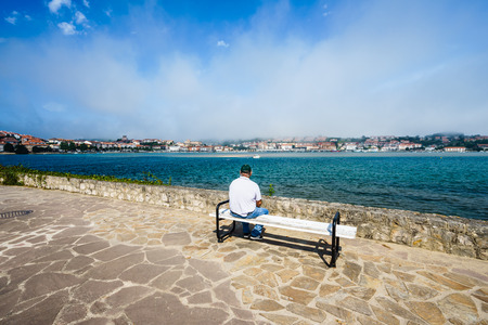 SAN VICENTE DE LA BARQUERA,CANTABRIA,SPAIN - 31 AUGUST,2016: Rear view of unrecognizable tourist sitting on bench and watching bay.Copy spaceのeditorial素材
